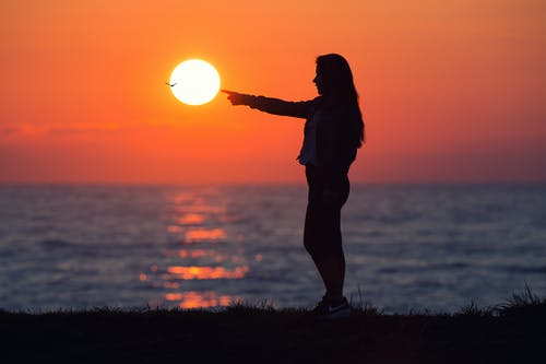woman pointing at sunset with water in the background