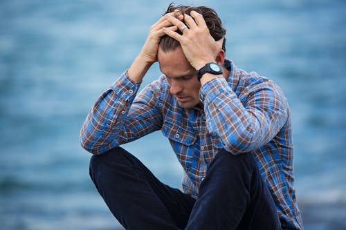 man with his hands on his head by water